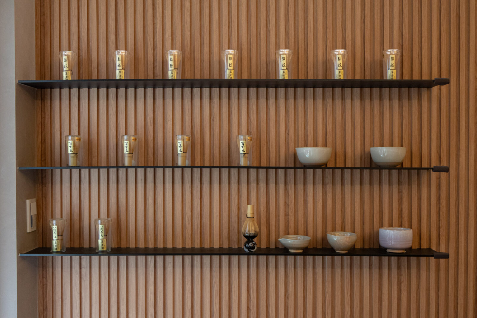 店內木質展示牆，陳列多支茶筅、茶碗與抹茶器具，呈現手刷抹茶專門店的日式茶文化氛圍。