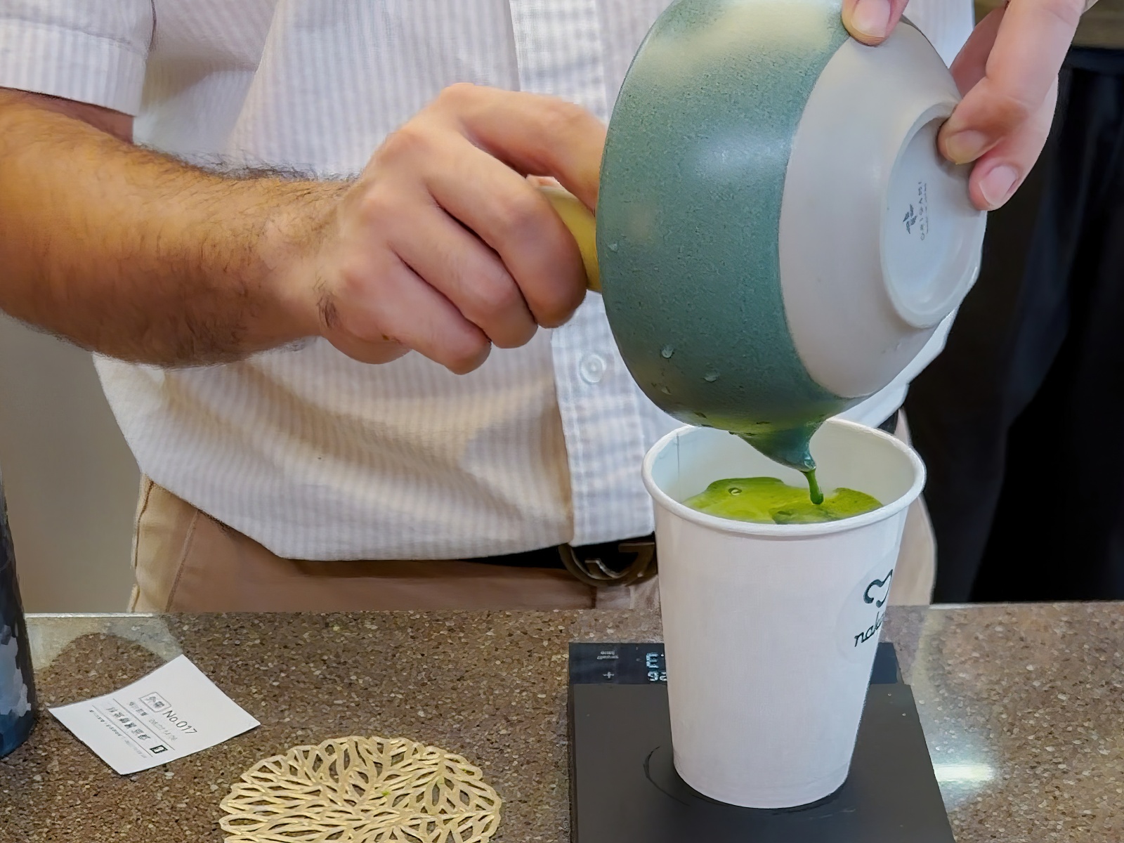 店員將現刷抹茶倒入外帶杯中，呈現手刷抹茶飲品的製作過程。