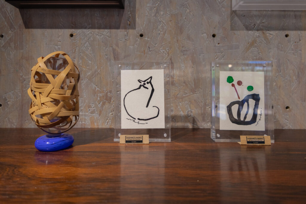 店內藝術選物展示，陳列竹編作品與小幅插畫，其中包含貓咪圖畫與抽象畫作。