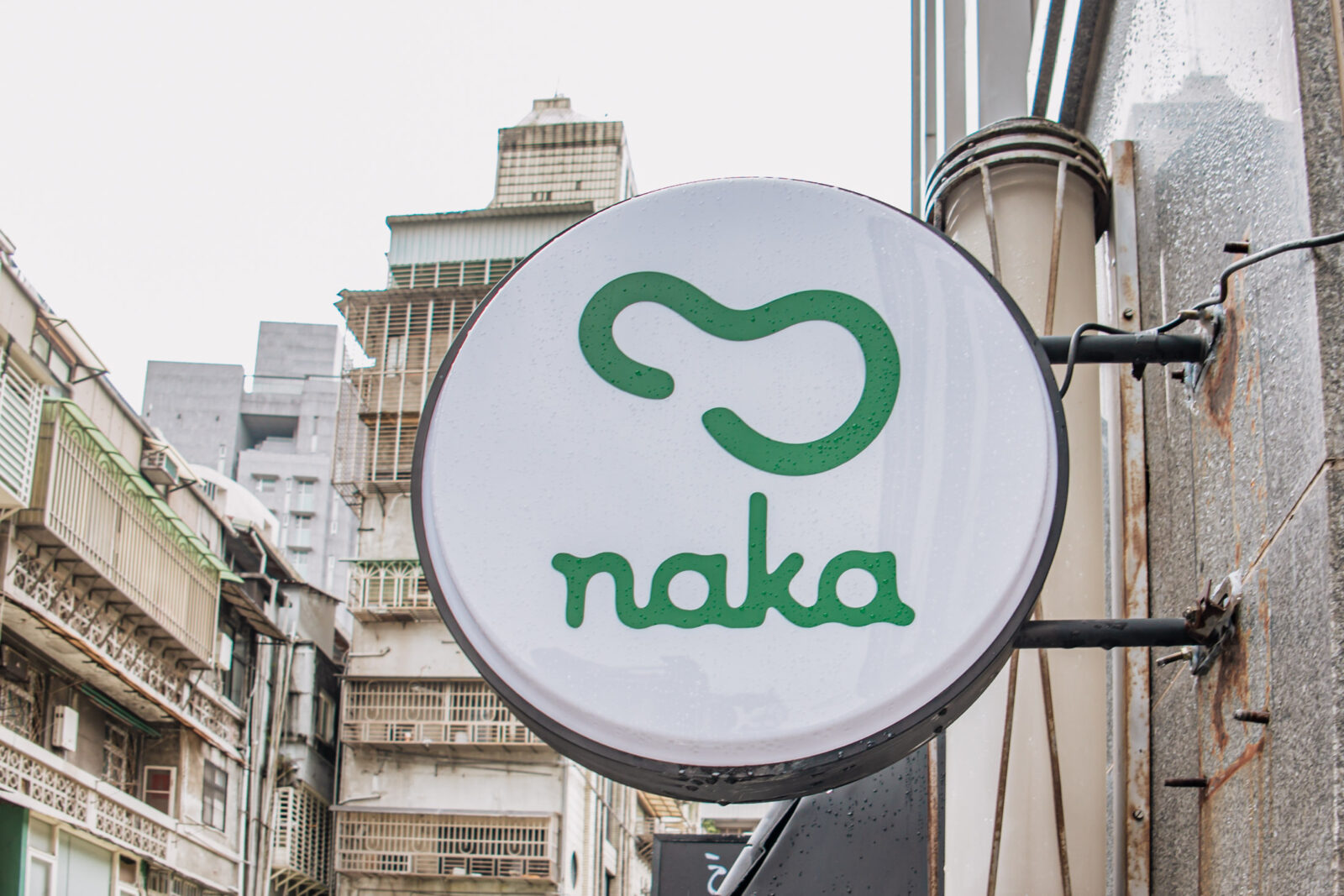 Naka Matcha 店外圓形招牌，白底綠色品牌 Logo，巷弄中相當醒目。