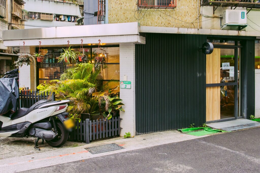 店門口，以深色直條外牆搭配木質入口設計，低調簡約，營業資訊掛在玻璃門上。
