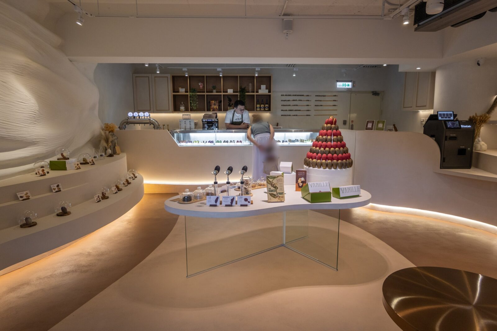 Maison Vanille 店內空間，以奶油白與流線曲面設計為主，中央設有香草與食材展示區，後方為瑪德蓮甜點櫃。