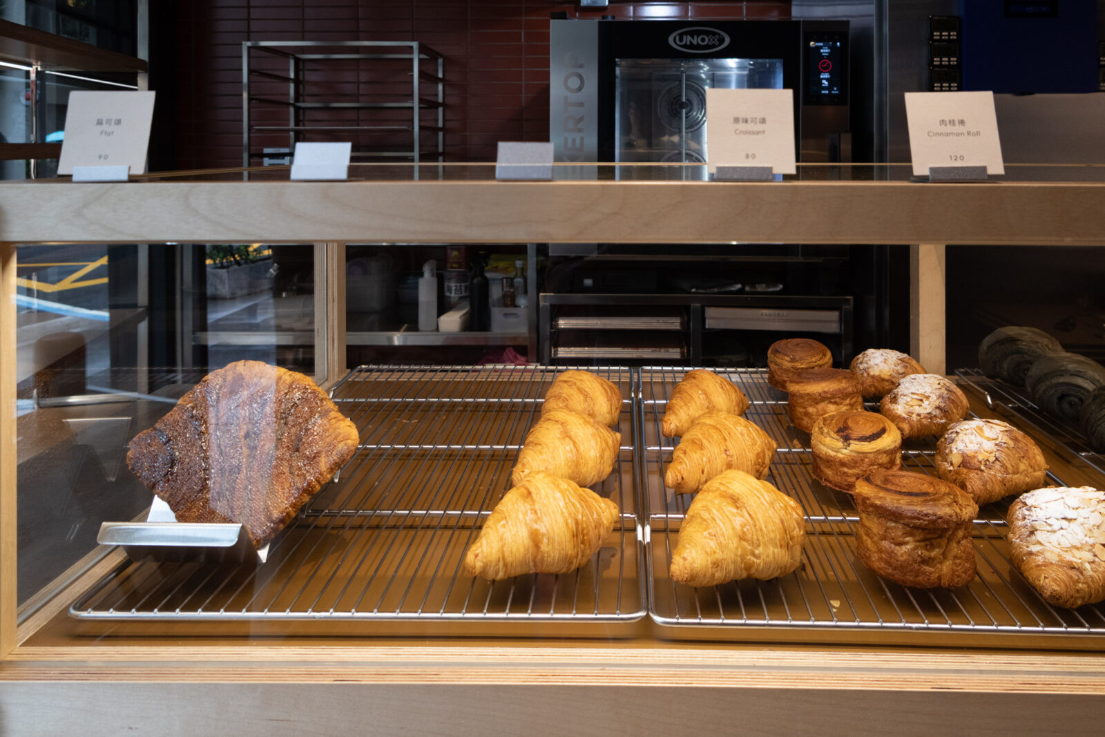 Muhei Bakery 暮黑烘焙可頌櫃，金黃原味可頌、肉桂捲與多款丹麥麵包整齊陳列於烤架上
