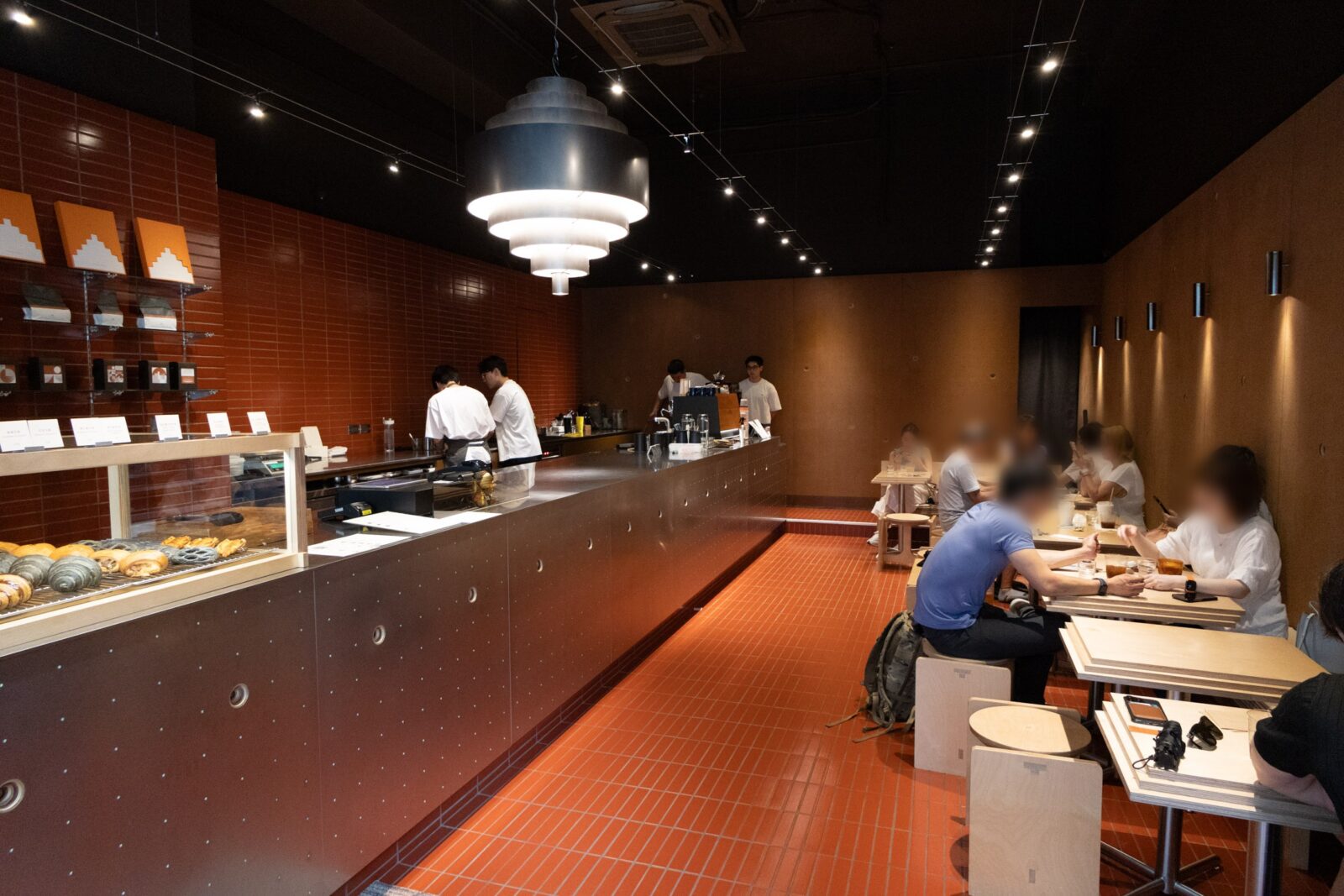 Muhei Bakery 暮黑烘焙店內空間，橘紅色地磚、金屬吧檯與淺色木桌椅構成狹長型內用區