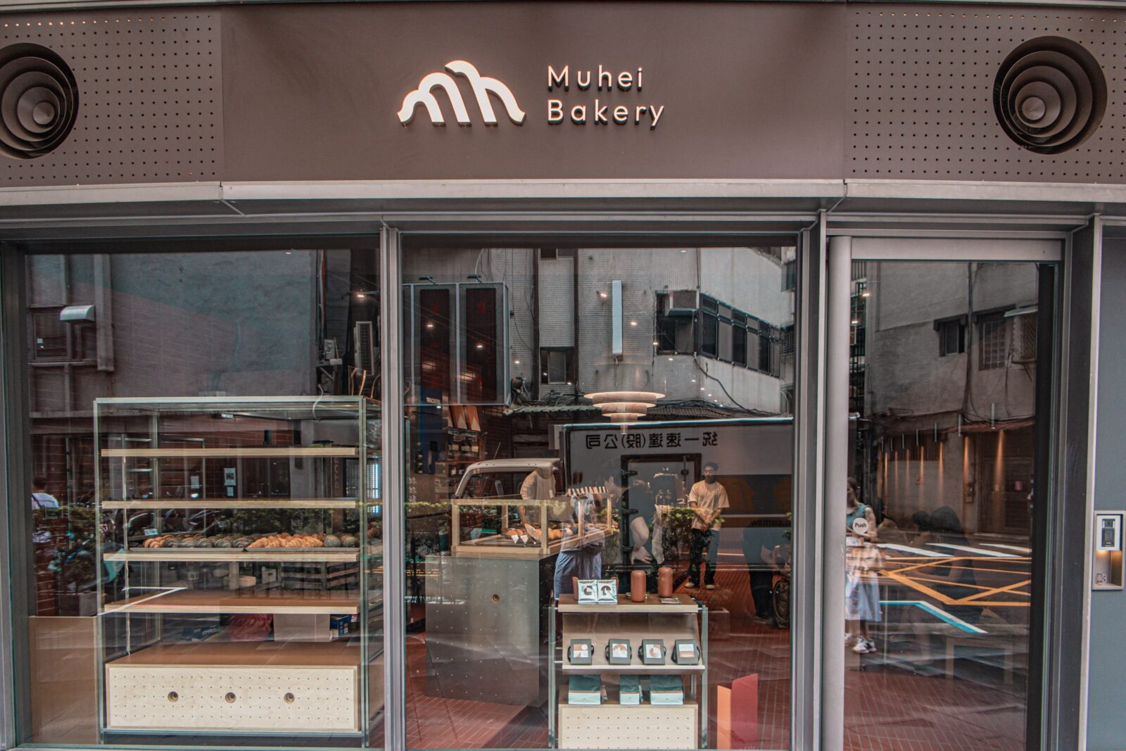 Muhei Bakery 暮黑烘焙店面，大片落地玻璃窗可看見可頌展示櫃與磚紅色店內空間