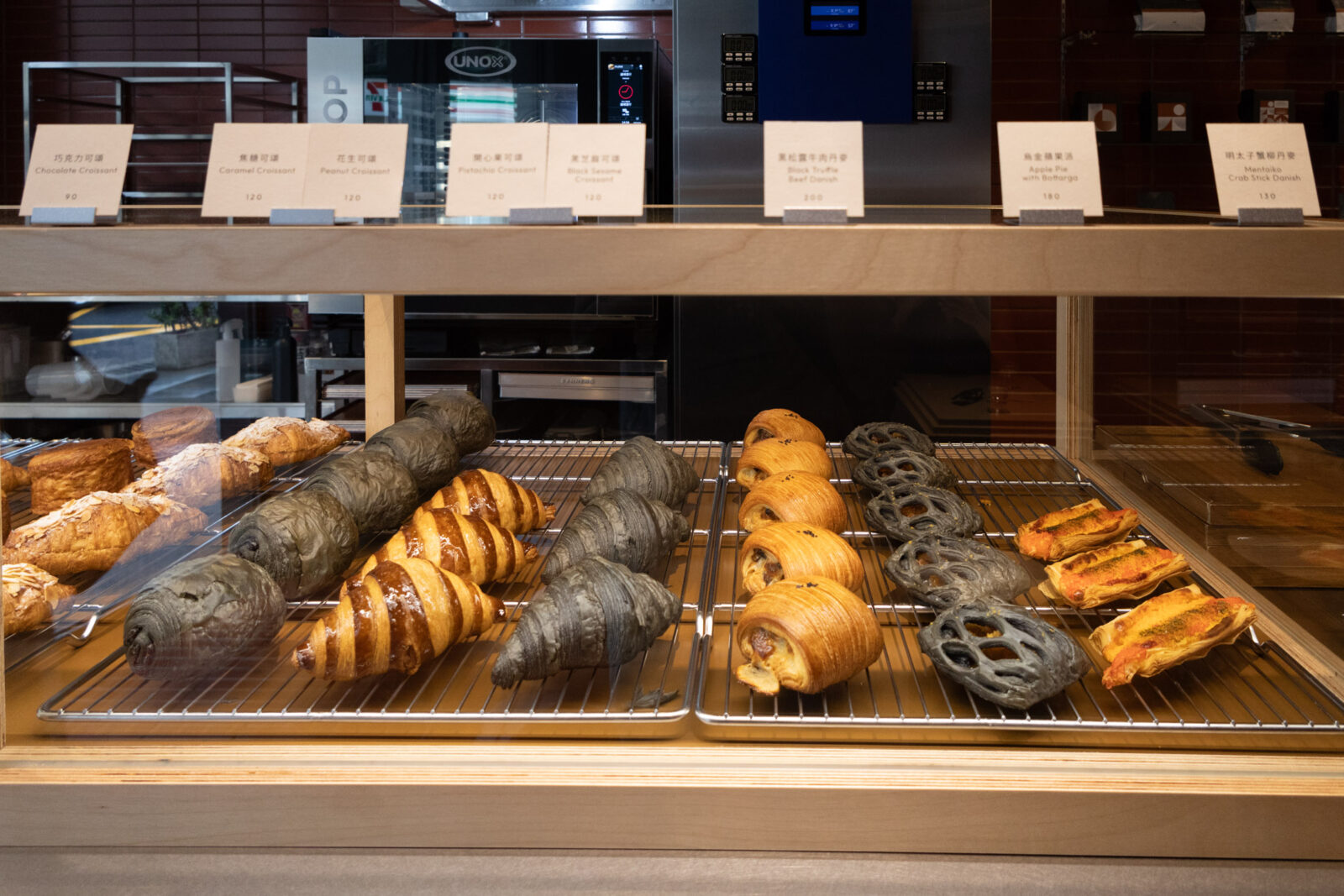Muhei Bakery 暮黑烘焙可頌櫃，多款金黃與竹炭色甜鹹可頌整齊陳列，口味與價格標示於上方